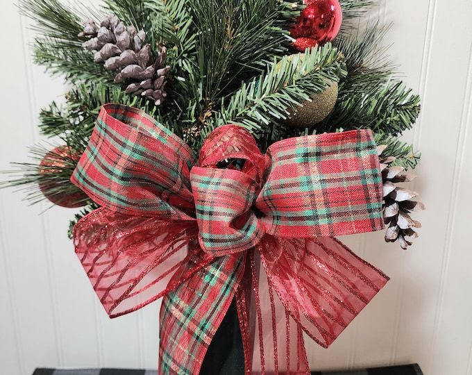 a christmas tree decorated with red and green plaid ribbon, pine cones and evergreen branches