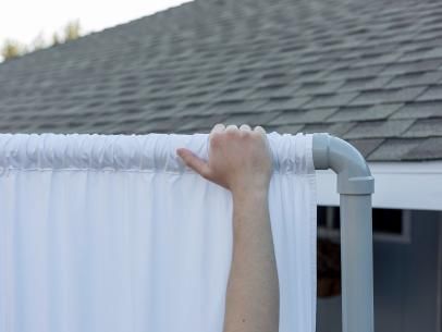 a hand that is on top of a curtain near a roof and window sill