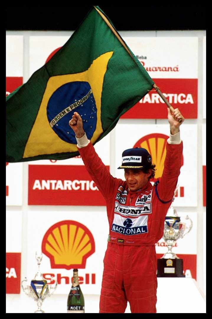 a man holding up a flag on top of a race track with his hands in the air