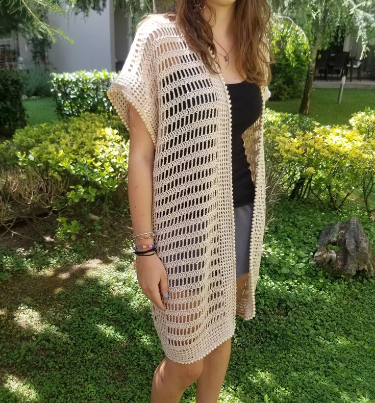 a woman standing in the grass wearing a crochet cardigan