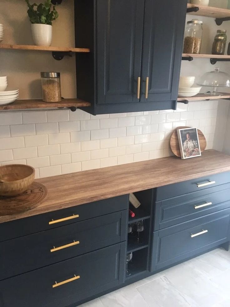 a kitchen with black cabinets and white subway backsplash, wood counter tops and brass pulls