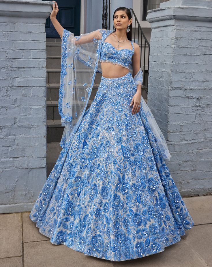 This lehenga set features powder blue three-dimensional floral embroidery, highlighted with crystals, pearls, and sequins on an ivory base. The waist of the blouse is scalloped and shows crystal drops. It is paired with a four-sided embroidered dupatta.From Seema Gujral's For the love of London collection. DELIVERY TIMEPlease allow 8-12 weeks for your outfit to arrive. FABRIC DETAILSNet Professional cleaning only. Pale Blue Lehenga, Pretty Indian Outfits, Wedding Reception Lehenga For Bride, Blue Glamorous Lehenga For Reception, Blue Sequined Sets For Reception, Glamorous Blue Lehenga For Festive Occasions, Glamorous Blue Festive Lehenga, Glamorous Floral Embroidery Wedding Sets, Glamorous Wedding Sets With Floral Embroidery