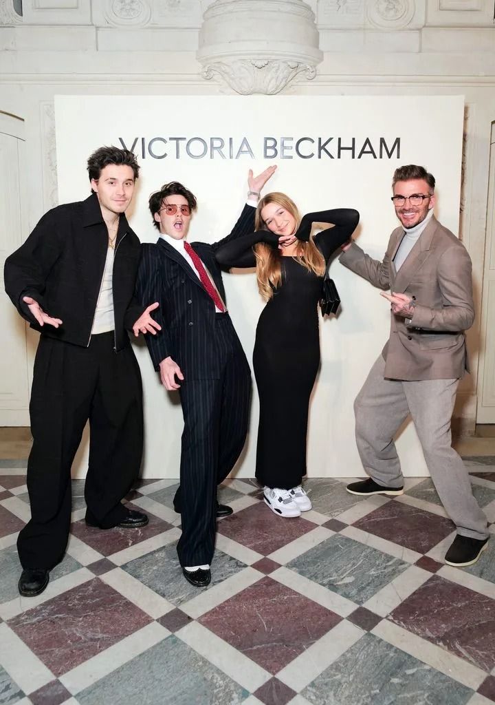 four people posing in front of a victoria beckham sign