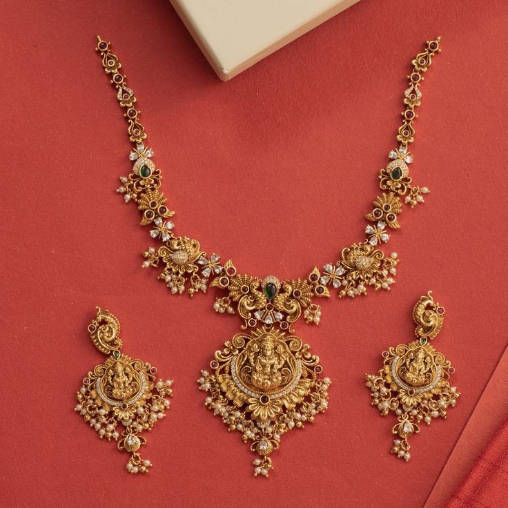 Description: This alluring necklace set from Tarinika features handcrafted designs decorated with temple elements surrounded with peacocks and flower motifs made of CZ stones and pearls on an antique gold base. Style this intricate temple set with any ethnic outfit. Details & Specifications:Materials used: Brass Alloy with Antique platingWeight - Necklace: 67 gms, Earrings: 29 gmsLength - Necklace: 19.5 cms, Earrings: 7.5 cmsMake it customWant to make it a custom necklace? Sure! Reach out to us Gold Necklace Set With Pearls, Antique Simple Necklace, Antique Gold Set Designs, Intricate Gold Necklace, Gold Necklace Designs For Bride, Gold Necklace With Earrings Set, Necleses Jewelry Gold Indian Latest, Temple Necklace Jewellery, Tarinika Jewellery