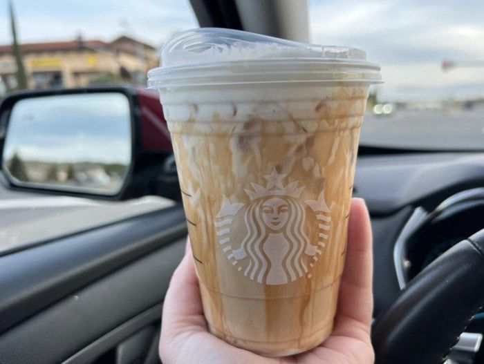 a person holding up a cup of coffee in their hand next to the steering wheel of a car