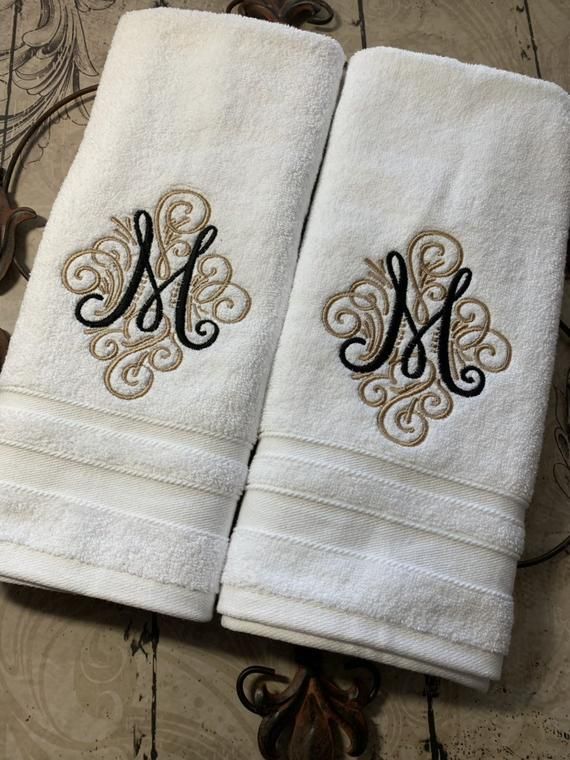 two white towels with black and gold monogrammed letters on them sitting on a table