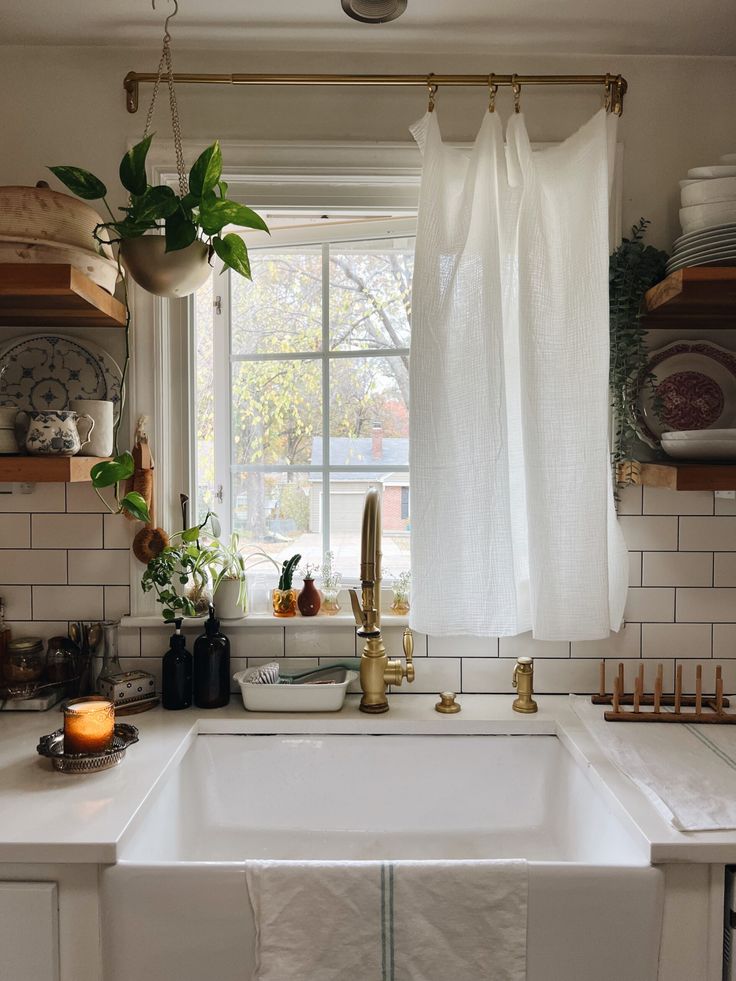 a white kitchen sink sitting under a window next to a potted plant and candle