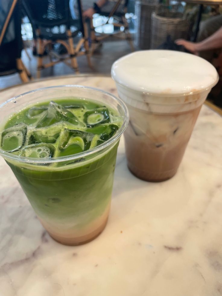 two drinks sitting on top of a table next to each other, one green and the other white