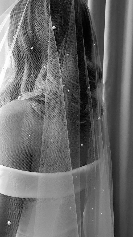 the back of a woman's head with a veil over her shoulder and pearls on it