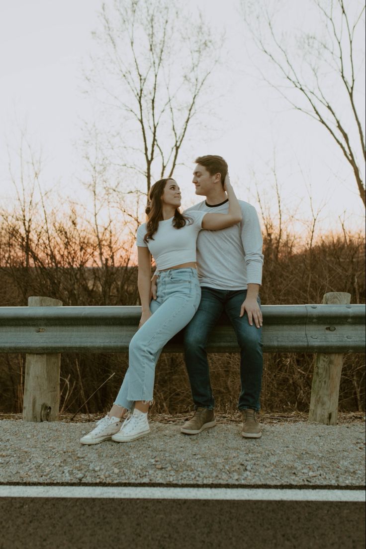 a man and woman sitting on top of a bench next to each other in front of trees