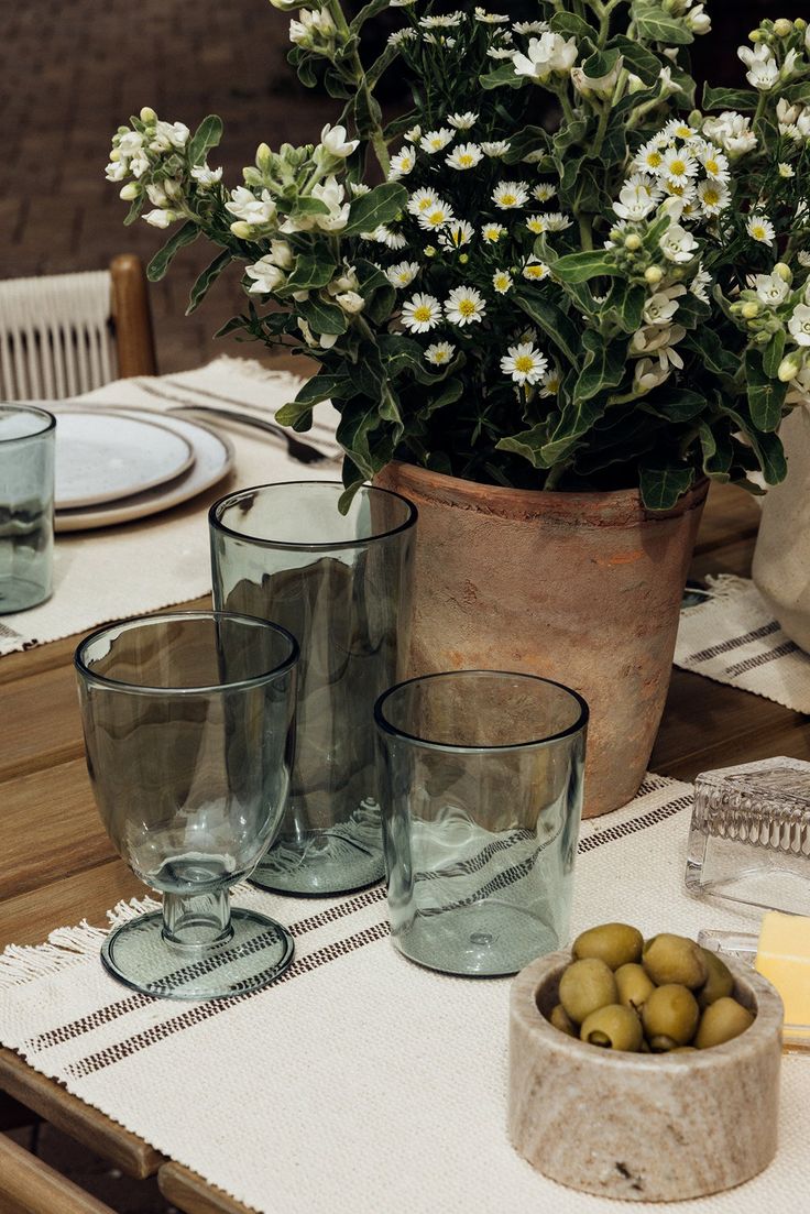 the table is set with glasses, plates and vases filled with green olives