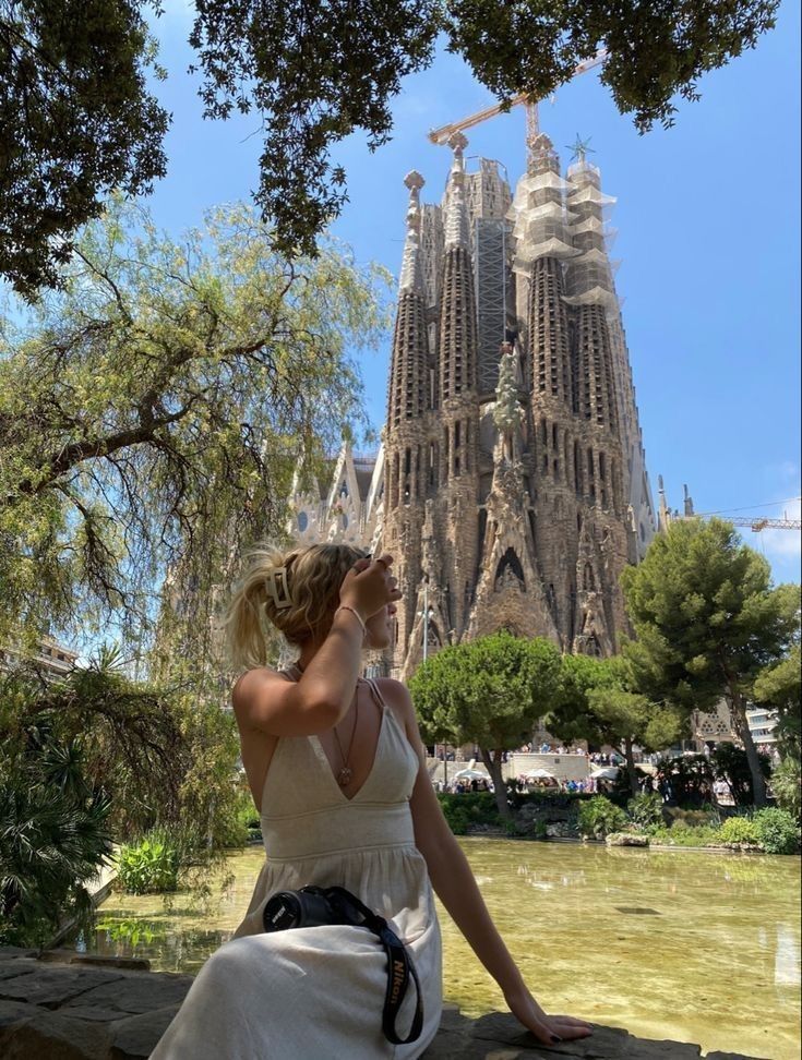 a woman in a white dress is sitting on a wall looking at the spires