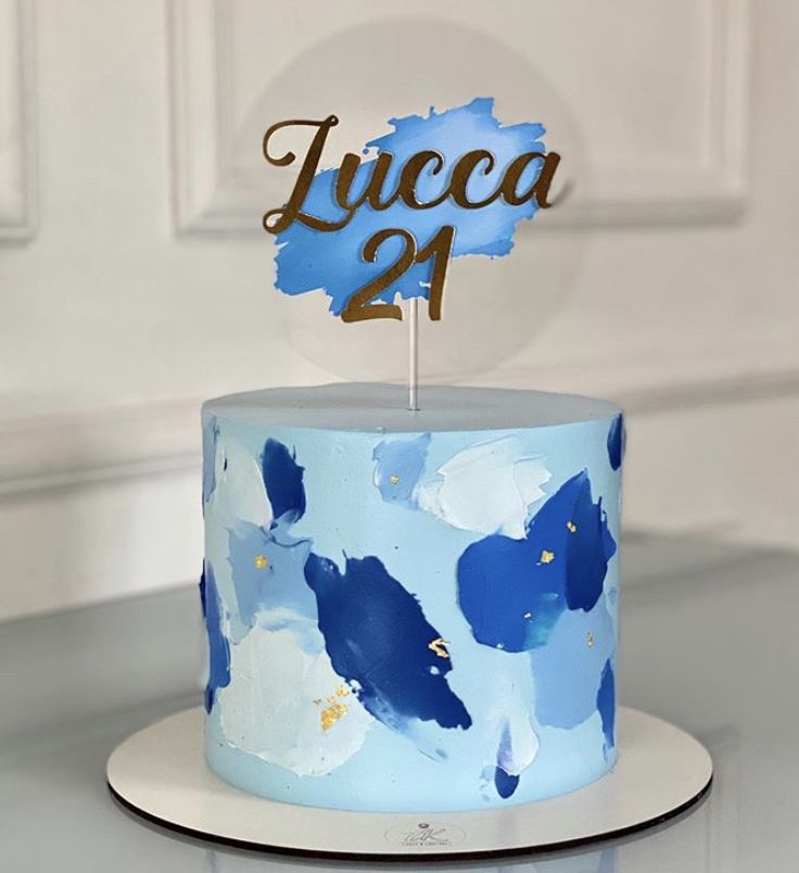 a blue and white cake with the number twenty four on it's top is decorated with gold lettering