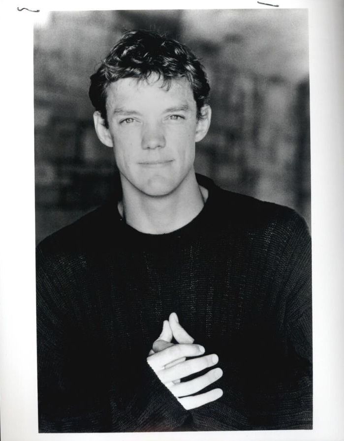 a black and white photo of a man with his hands folded in front of him