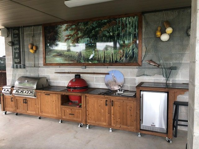 an outdoor kitchen with wood cabinets and stainless steel appliances on the counter top, in front of a painting