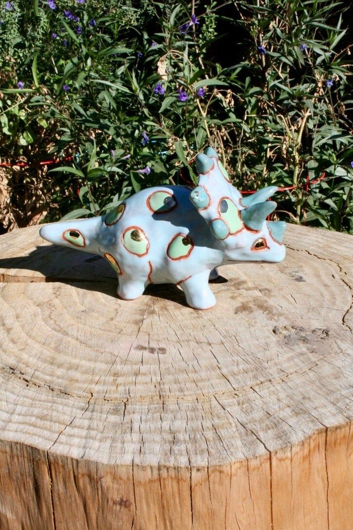 two small ceramic animals sitting on top of a tree stump in front of some bushes