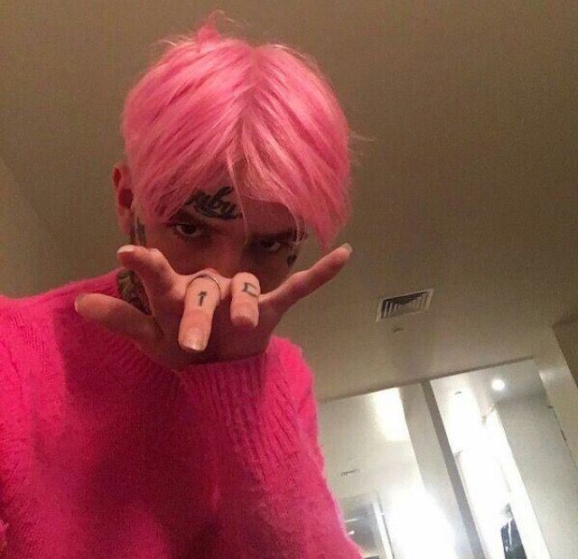 a person with pink hair and tattoos making a peace sign