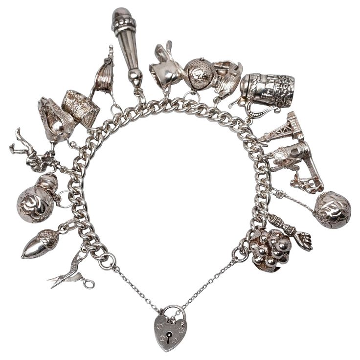 This English 1950s heavy sterling silver bracelet has 17 large three-dimensional charms and opens or closes with a heart shaped padlock on a little safety chain. Some of the charms have moving or opening parts. The windmill really turns, the lid of the beer mug opens, the ship opens up, the leaves on the orange are separate from the orange, the bellow bellows, the treasury chest opens, the corn has loose leaves and the scissors 'cut'. Three of them are European solid silver pendants: the acorn ( German Silver Jewelry, Long Pendant, 925 Silver Jewelry, Silver Pendants, Gold Charm, Heart Charm Bracelet, Charm Jewelry, Vintage Sterling Silver, Sterling Silver Bracelets