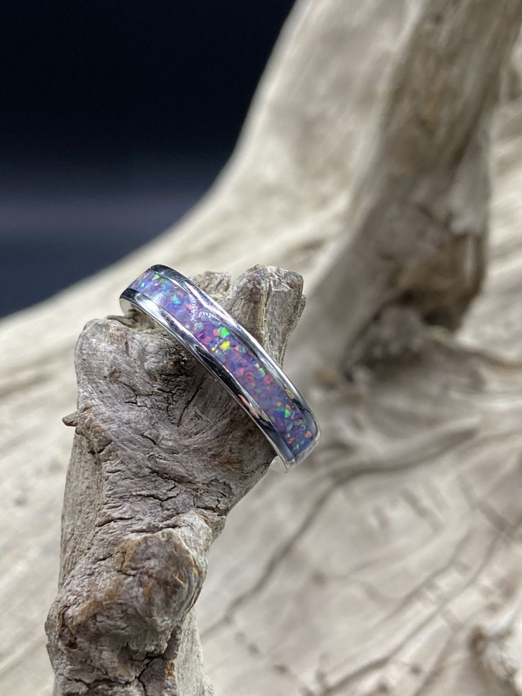 This beautiful handcrafted Stainless Steel comfort band is a real conversation starter! It features a Lavender Opal inlay in the center of the ring. The crushed Opal is placed by hand, incased in resin, and then finished and polished to a brilliant shine. Each ring I make is truly unique and no two are ever the same. These rings are made to order and are available in several sizes. Please allow 3-5 days for me to complete your ring. I do custom orders and if you have a different ring material or Opal Inlay Ring Gift, Opal Ring With Inlay Perfect For Gifts, Gift Opal Inlay Ring, Adjustable Thick Band For Gift, Adjustable Thick Band Gift Bands, Unique Opal Ring With Inlay For Gift, Oval Opal Ring With Inlay For Gift, Diy Resin Ring, Opal Wedding Band