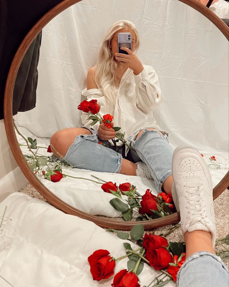 a woman taking a selfie in front of a mirror with roses on the floor