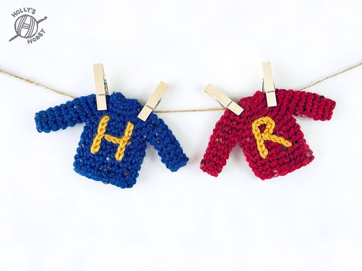 two crocheted sweaters hanging from clothes pins on a string with clothes pins attached to them