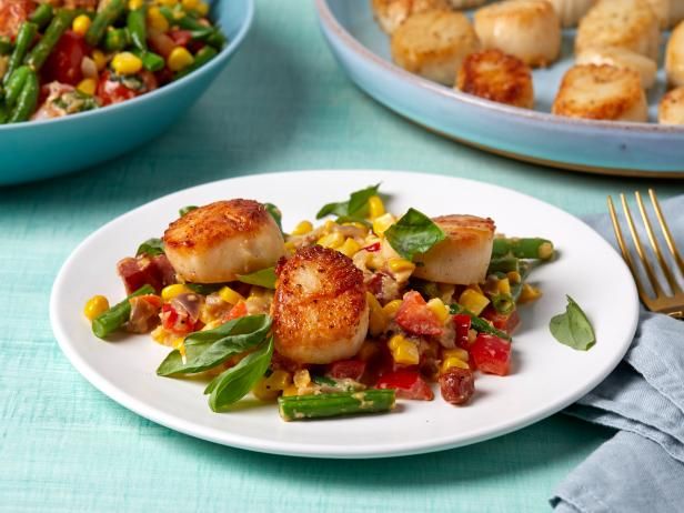 scallops with corn and vegetables on a white plate next to blue plates filled with food