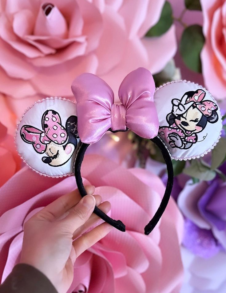 a person holding onto a minnie mouse headband with pink flowers in the back ground