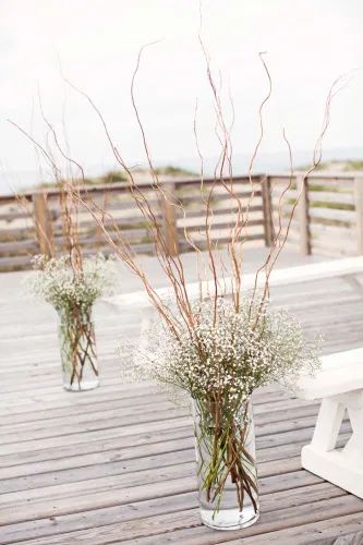 two vases filled with white flowers sitting on top of a wooden table next to a bench