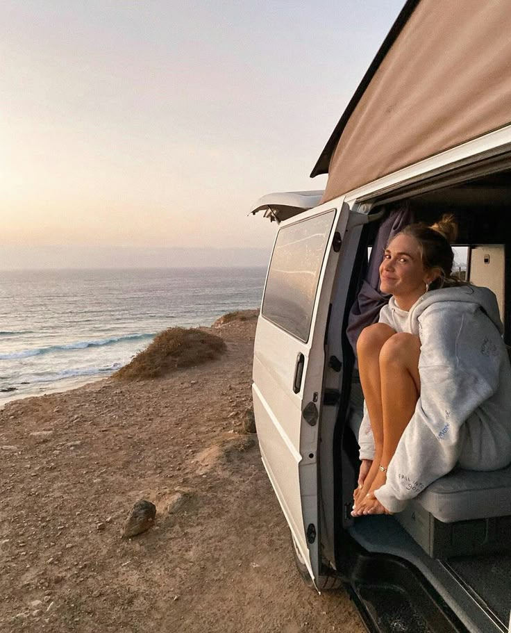 a woman sitting in the back of a van next to the ocean