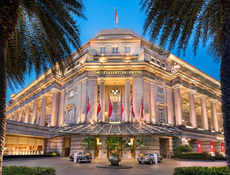 a large building with many flags on it's roof and palm trees in front