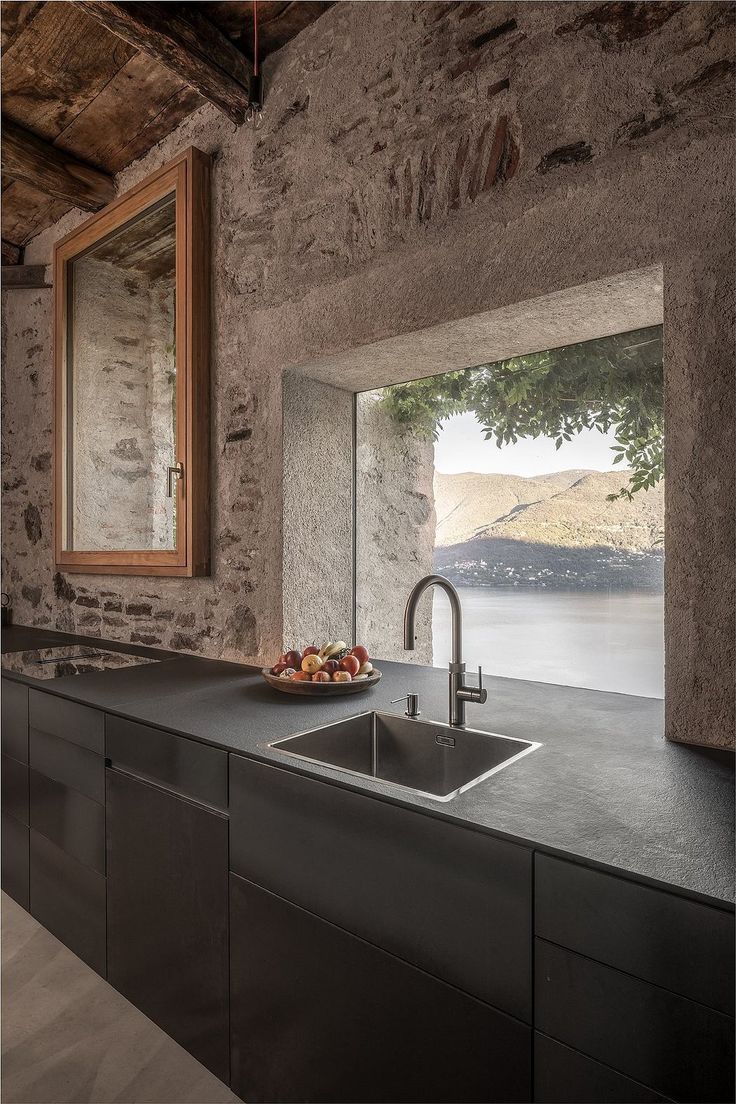 a modern kitchen with stone walls and an open window overlooking the water is pictured in this image