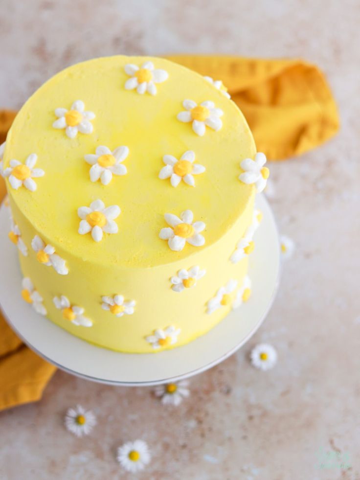 a yellow and white cake with daisies on it sitting on top of a plate