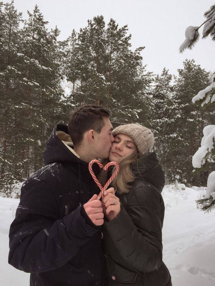 a man and woman standing in the snow holding a heart shaped lollipopo