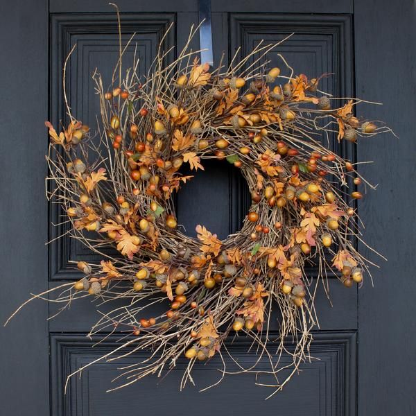 a wreath is hanging on the front door with autumn leaves and berries around it,