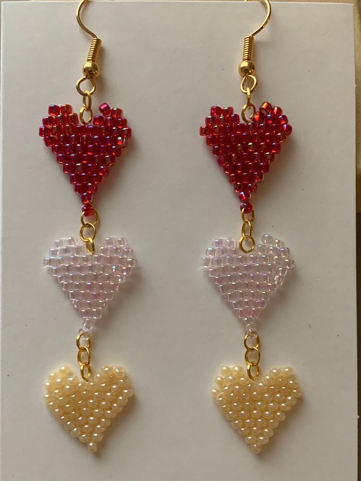 two heart shaped beads hanging from gold chains on a white card with red and yellow beading