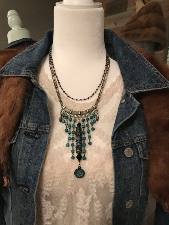 The fabric and ribbon wrapped bead with its little butterfly charm makes this boho beauty unique and fun. It hangs from a totally cool tribalistic pendant that is loaded with detail, which I paired with pieces of teal wooden linked beads. It's finished off with double strands of chain and tiny glass beaded chain. Thanks for looking! Bohemian Black Beaded Dangle Necklaces, Bohemian Beaded Necklaces With Dangling Beads, Bohemian Multi-strand Black Bead Jewelry, Bohemian Black Beaded Dangle Jewelry, Black Bohemian Beaded Necklaces, Bohemian Multi-strand Beaded Necklace With Black Beads, Bohemian Turquoise Dangle Beaded Necklaces, Bohemian Turquoise Beaded Dangle Necklaces, Bohemian Beaded Dangle Necklace