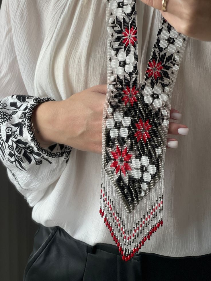 a close up of a person wearing a white shirt and black pants holding a beaded tie