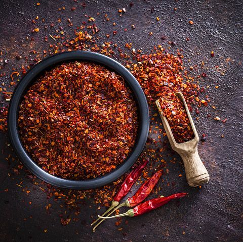 a bowl filled with red peppers next to a wooden spoon and pepper grinder on a black surface