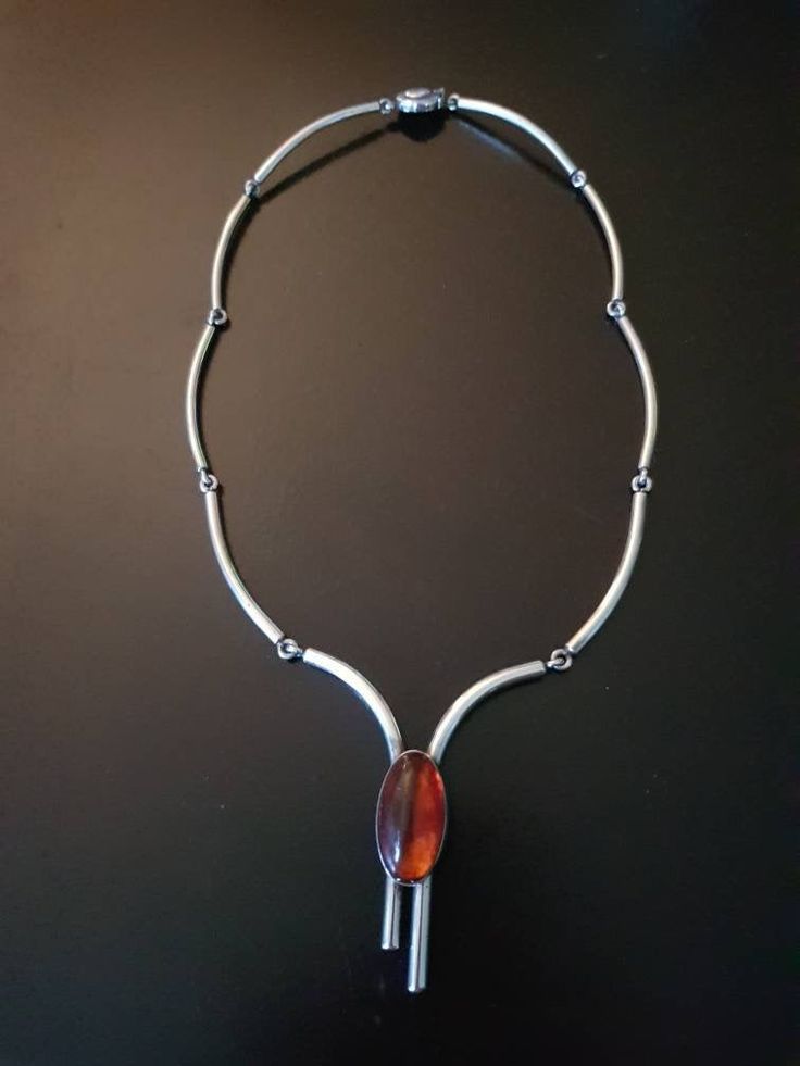 a silver necklace with an orange glass bead hanging from it's center, on a black surface