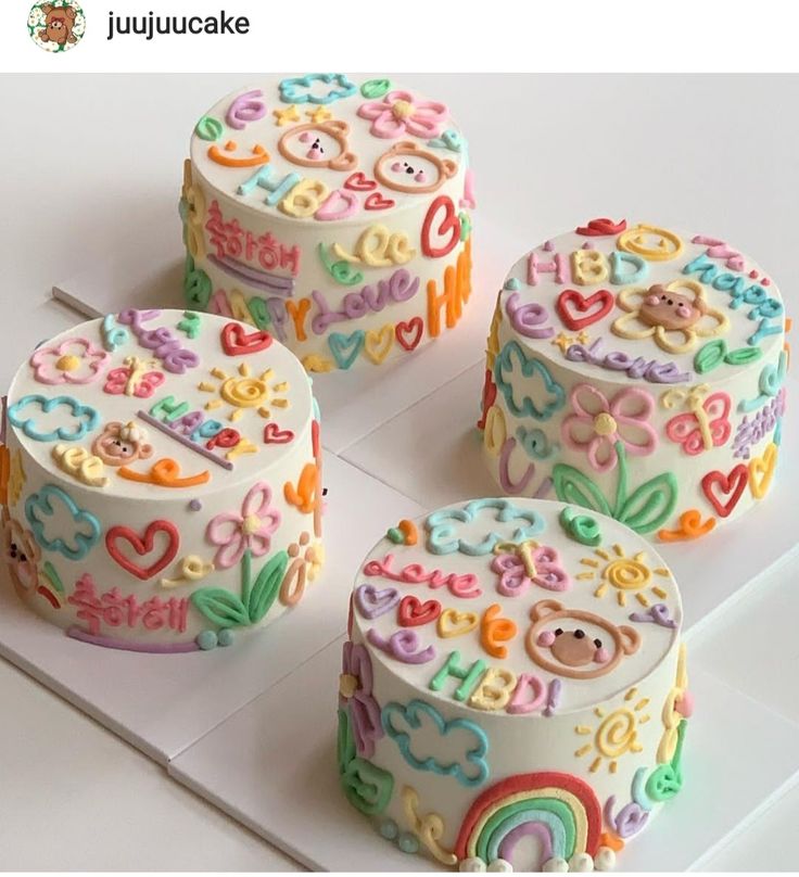 four decorated birthday cakes sitting on top of a white table with rainbows and hearts