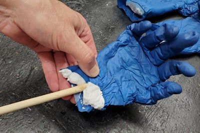 a person wearing blue gloves and holding a wooden stick