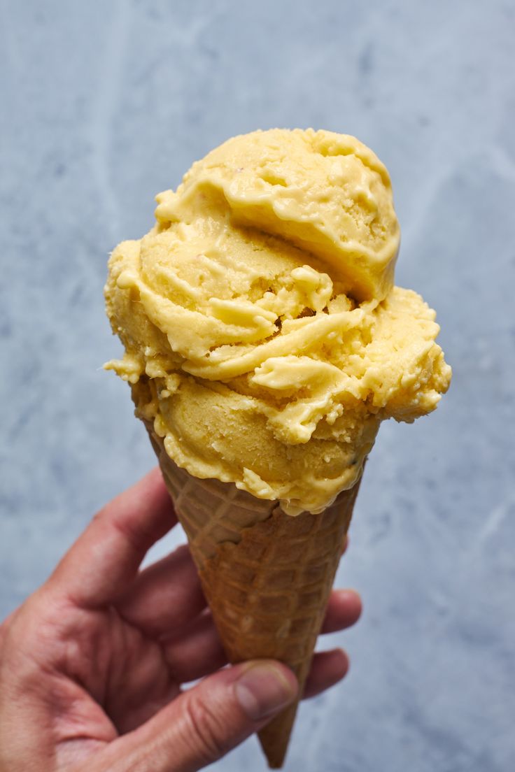 a hand holding an ice cream cone with yellow icing