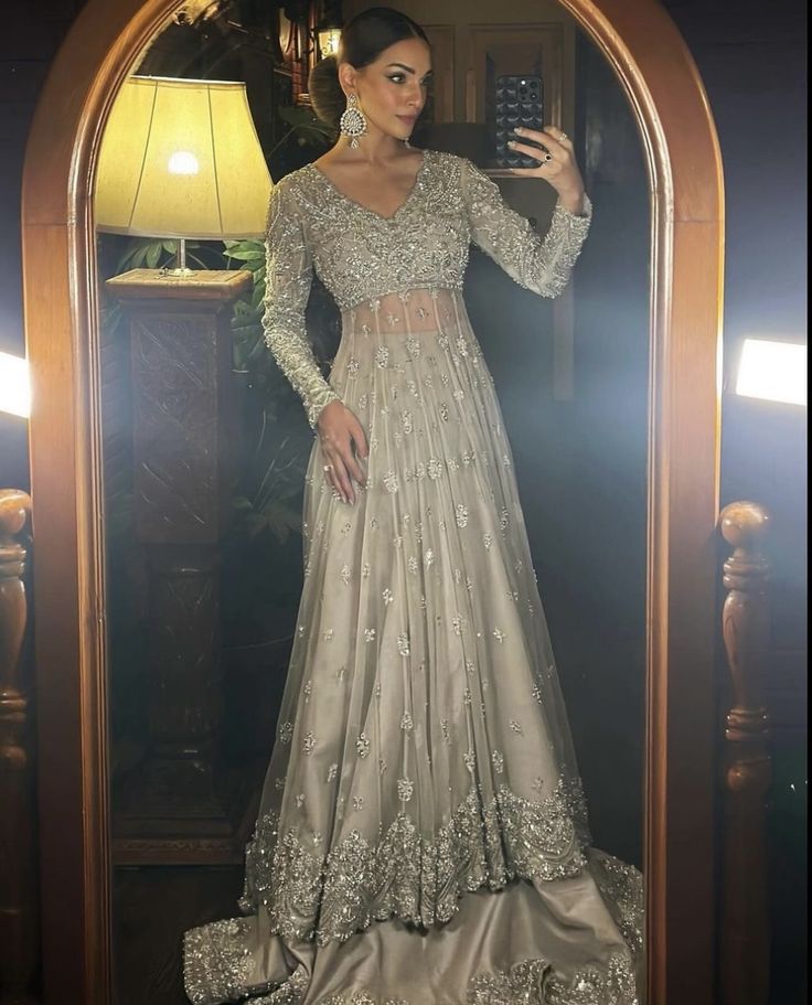 a woman taking a selfie in front of a mirror wearing a silver gown and matching earrings