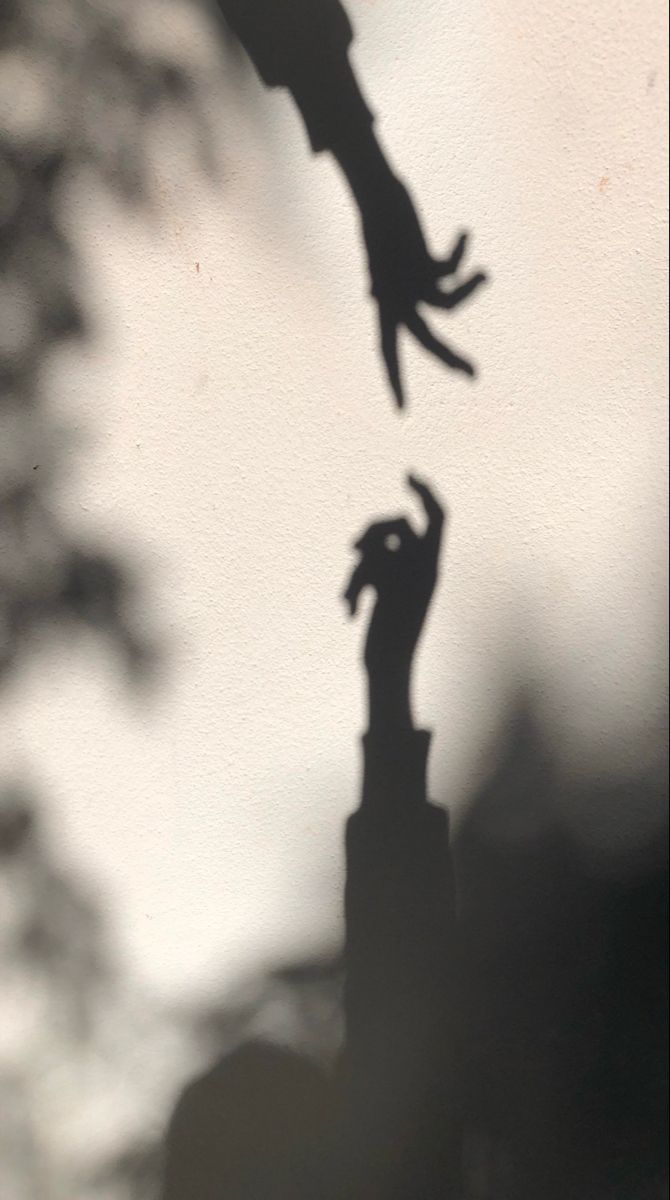 the shadow of two people reaching up into the air to grab something out of their hands