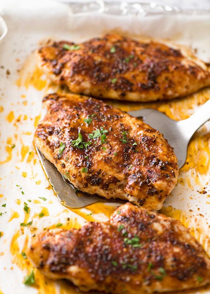 oven baked chicken breast on a baking sheet with a spatula in the foreground and text overlay that reads oven baked chicken breast