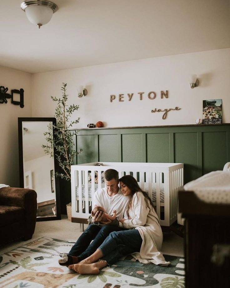 a man and woman sitting on the floor in front of a crib looking at a cell phone