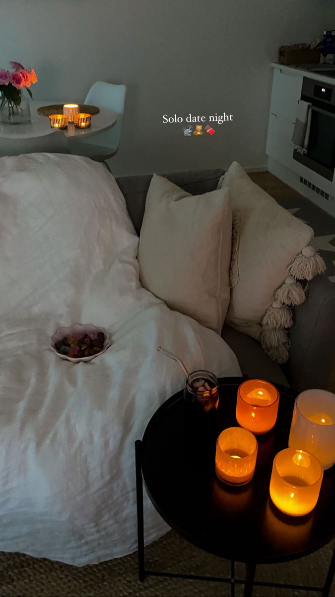 candles are lit in front of a bed with white sheets and pillows on the floor