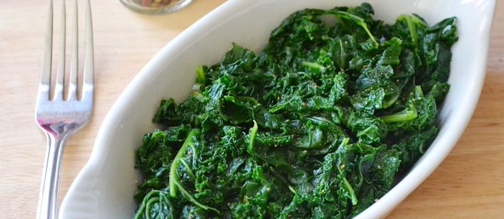 a white bowl filled with greens next to a fork