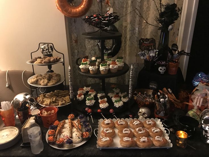 an assortment of desserts and snacks on a table in front of a wall decorated with halloween decorations