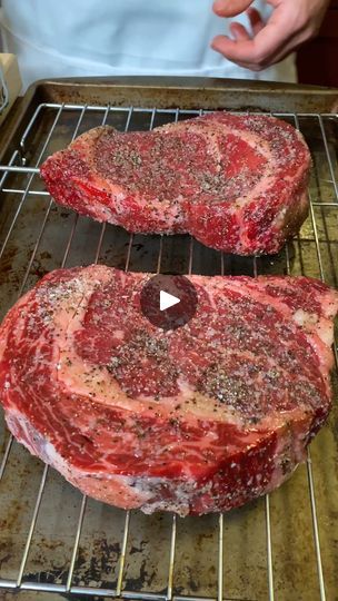 two uncooked steaks sitting on top of a metal rack next to each other